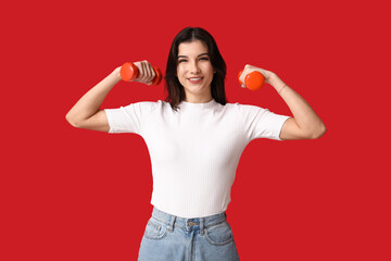 Wall Mural - Young woman exercising with dumbbells on red background. Feminism concept