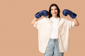 Wall Mural - Young woman in boxing gloves celebrating success on beige background. Feminism concept