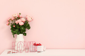 Vase with bouquet of roses and gift box on white cabinet near pink wall, closeup. Valentine's Day celebration