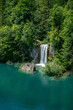 Nationalpark Plitvicer Seen, Kroatien. Wasserfall umrahmt von Bäumen im Vordergrund ein See mit Felsen am Tag