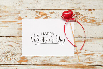 Card with text HAPPY VALENTINE'S DAY and heart on light wooden background