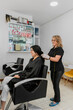 Mature hairdresser holding the hair of a young latina woman in the beauty salon.
