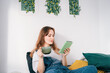 © okrasiuk - Young woman reading e-book on tablet reader in bed. Female relaxing with hot drink while reading an electronic book in cozy room. Mental health recovery, Personal growth. Hobby, Leisure time alone.