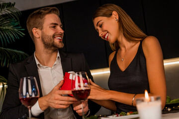 Wall Mural - Young romantic couple sitting at home kitchen and man giving gift box his female during romantic dinner