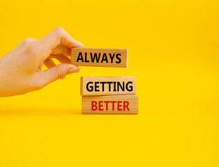 Always getting better symbol. Wooden blocks with words Always getting better. Beautiful yellow background. Businessman hand. Business and Always getting better concept. Copy space.