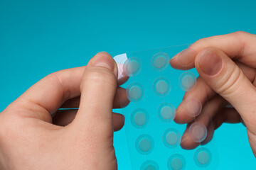 Close-up round acne patch on finger on blue background. Acne patches for treatment of pimple and rosacea close-up. Facial rejuvenation cleansing cosmetology