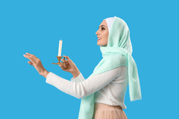 Wall Mural - Young Muslim woman with burning candle on blue background. Islamic New Year celebration