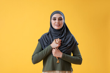 Wall Mural - Young Muslim woman with prayer beads on yellow background. Islamic New Year celebration