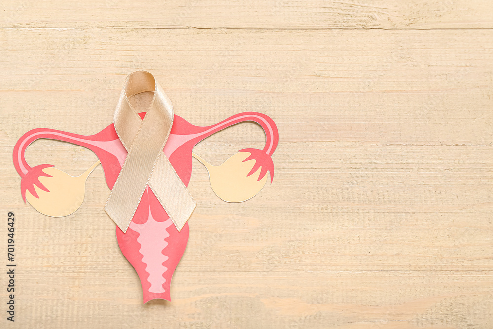 Beige ribbon with paper uterus on light wooden background. Cancer awareness concept