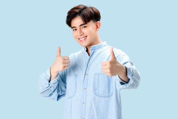 Happy young Asian smart man show  thumbs up over isolated blue background.