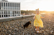 Lively pretty little girl wearing stylish yellow dress playing with dachshund dog on summer terrace of high-rise building. Happy childhood with love for pets. Copy space.