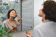 Beautiful middle-aged woman preparing to go out, doing her morning makeup routine and applying face powder with brush in front of mirror in the bathroom.