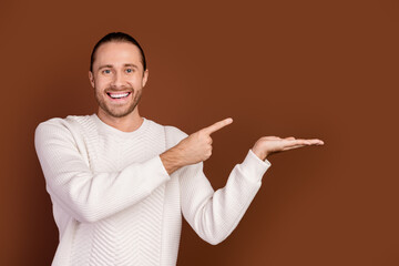 Wall Mural - Photo of excited positive man wear white sweater showing finger holding arm empty space isolated brown color background
