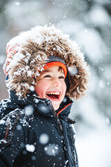 Wall Mural - Happy kid wearing warm clothes plays outdoors with snow in winter.