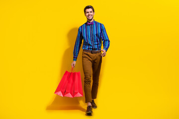 Poster - Full size photo of cool cheerful guy dressed striped shirt walking with shopping bags buy new outfit isolated on yellow color background