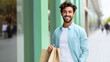 Handsome young man holding or carrying a shopping bag in his hand, walking on the city street, smiling and looking at the camera. Happy male customer buying on a discount from mall or retail store