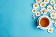 Flat lay image of chamomile tea in a white cup, with daisy flowers and dry tea on a blue background.