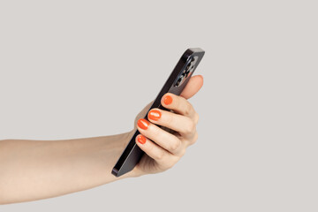 Closeup of woman hand using mobile phone reading news in internet, watching photo or video. Indoor studio shot isolated on gray background.