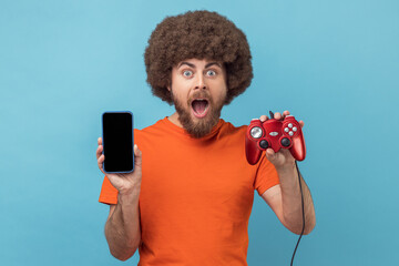 Wall Mural - portrait of surprised astonished man with afro hairstyle wearing orange t-shirt holding joystick and