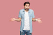 Portrait of unaware questioned man standing spreads palms, shrugs shoulders with perplexed expression, being indecisive, has no idea what happened. Indoor studio shot isolated on pink background.