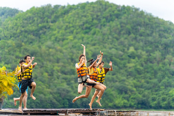 Wall Mural - Group of Young Asian man and woman friends with life vest jumping into the lake and swimming together. Happy People enjoy and fun outdoor lifestyle travel nature lake house on summer holiday vacation.