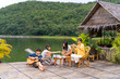 © CandyRetriever  - Young Asian man and woman enjoy outdoor lifestyle travel nature forest mountain on summer holiday vacation. Happy generation z people friends playing guitar and doing hobbies at lake house balcony.