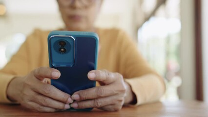 Senior woman using mobile phone touching scroll page app on mobile phone at room.Manager typing telephone alone watch film online.