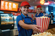 Smiling young woman working at a movie theater cafeteria holding a box of popcorn 