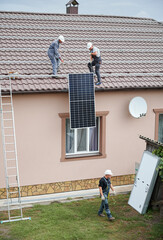 Wall Mural - Men workers lifting up photovoltaic solar modul on roof of house. Electricians in helmets installing solar panel system outdoors. Concept of alternative and renewable energy.