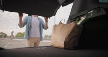 Young Man Opens Car Trunk And Takes Away Bags With Groceries