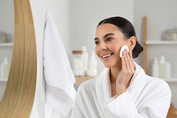 Poster - Beautiful woman removing makeup with cotton pad near mirror in bathroom, space for text