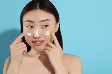 Wall Mural - Beautiful young woman with sun protection cream on her face against light blue background, space for text