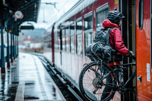 A Cyclist Carrying A Backpack, Lifting His Bicycle Onto A Train On A Rainy Day At The Station