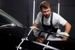 © Roman - Professional auto mechanic polishing or cleaning black automobile with rag. Manual car washing. In Auto service, man in uniform and gloves cleaning vehicle