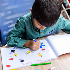 Smart Indian little boy perform thumb painting with different colourful water colour kit during the summer vacations, Cute Indian Kid doing colourful thumb painting drawing on wooden table