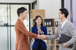 © ArLawKa - A successful professional Asian businessman and his business partner stand and shake hands while a woman stands behind them in a company conference room.