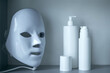 © andrey_orlov - Light therapy LED mask on a shelf next to facial skin care products.