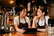Portrait of two smiling waitresses using tablet while working in cafe