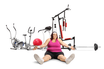 Wall Mural - Tired plus size woman in sportswear sitting on the ground in front of a fitness gear