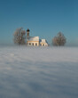Bavarian church of Raisting with trees and snow and mist during winter, snow field in the foreground, blue sky day, Bavaria Germany.