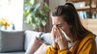 Female with respiratory illness sneezing due to allergies or flu, in living room with tissue and congestion, potentially facing health complications.