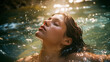 A young woman with her eyes closed partially submerged in water with small ripples. Sunlight is shining on the water, creating bright reflections and giving it a sparkling appearance. Dreamy mood.