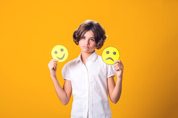 Upset girl holds emoticons with happy and sad emotions.