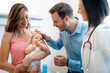 © Dorde - Happy proud father and mother holding adorable newborn baby standing with a smiling female doctor during visit. Female pediatrician with cheerful parents and a baby.