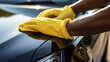 © Margo Alexa - hand of a man in a yellow glove cleaning a car with a microfiber cloth, washing and polishing the surface of the car