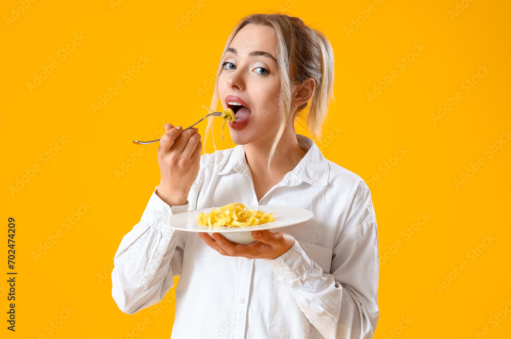 Young woman eating tasty pasta on yellow background