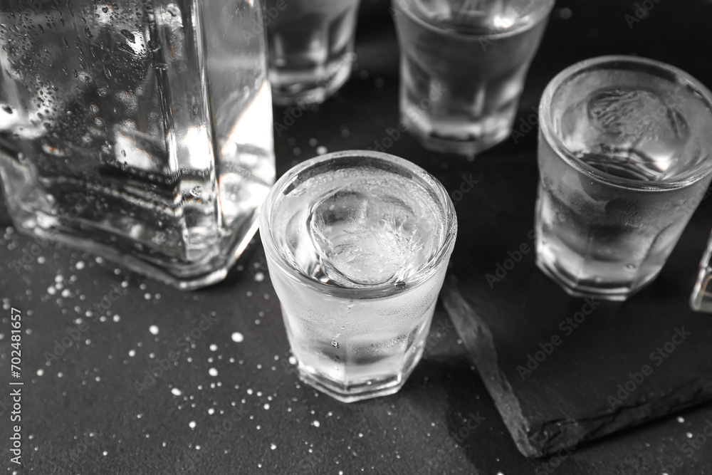 Shots and bottle of vodka with ice cubes on black background