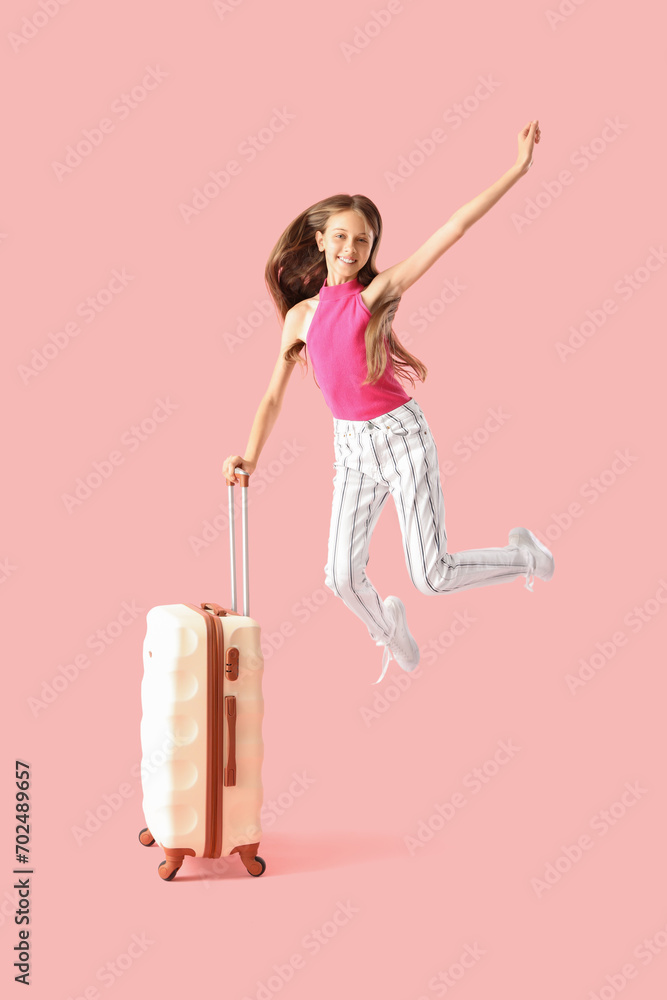 Happy little girl with suitcase jumping on pink background