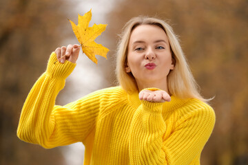 Canvas Print - Beautiful woman with autumn leaf blowing kiss outdoors