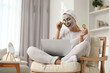 Young woman with face mask and cucumber slices using laptop at home. Spa treatments